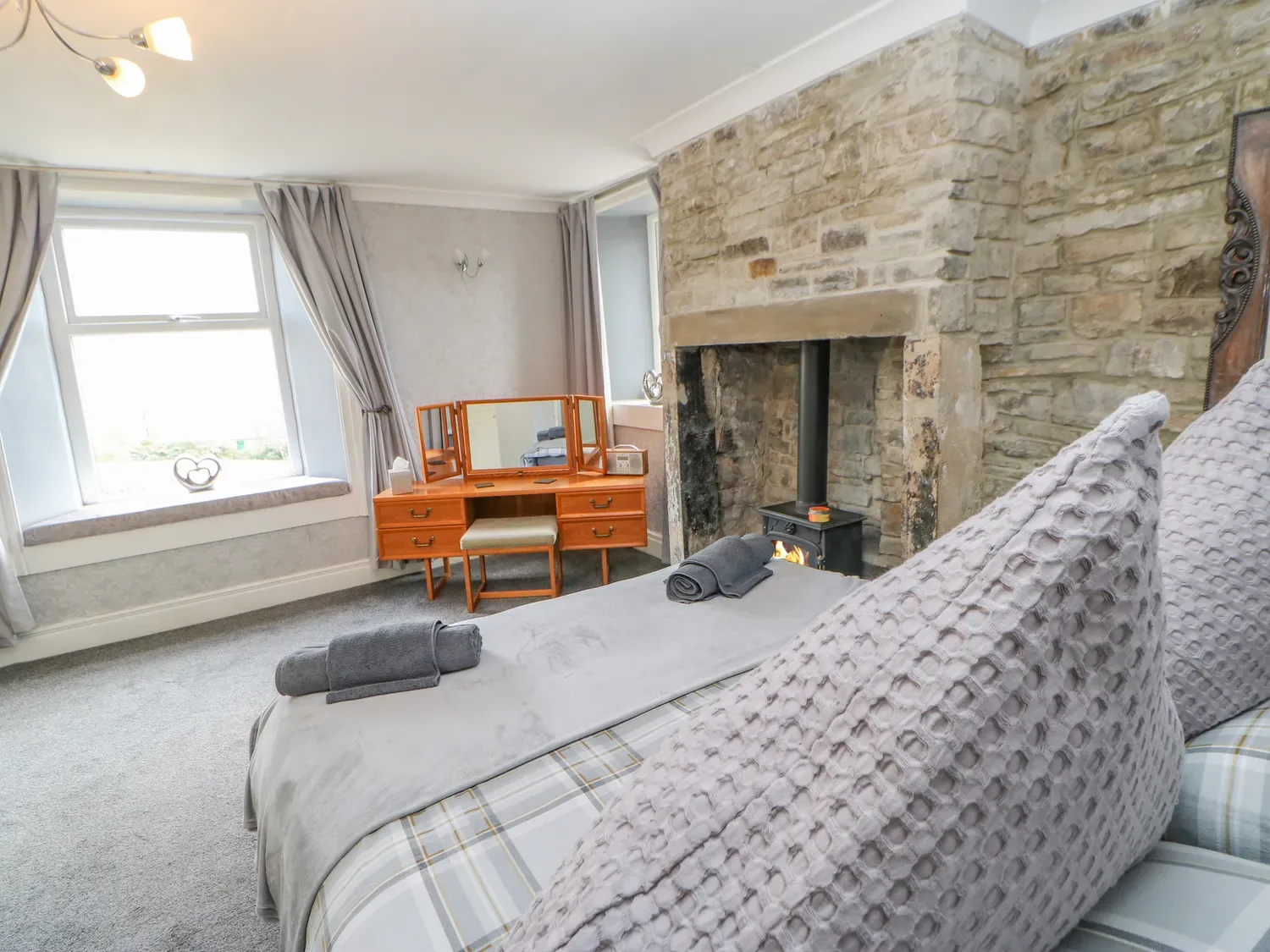 Un dormitorio con una cama, un tocador, una ventana con cortinas y una chimenea de piedra.
