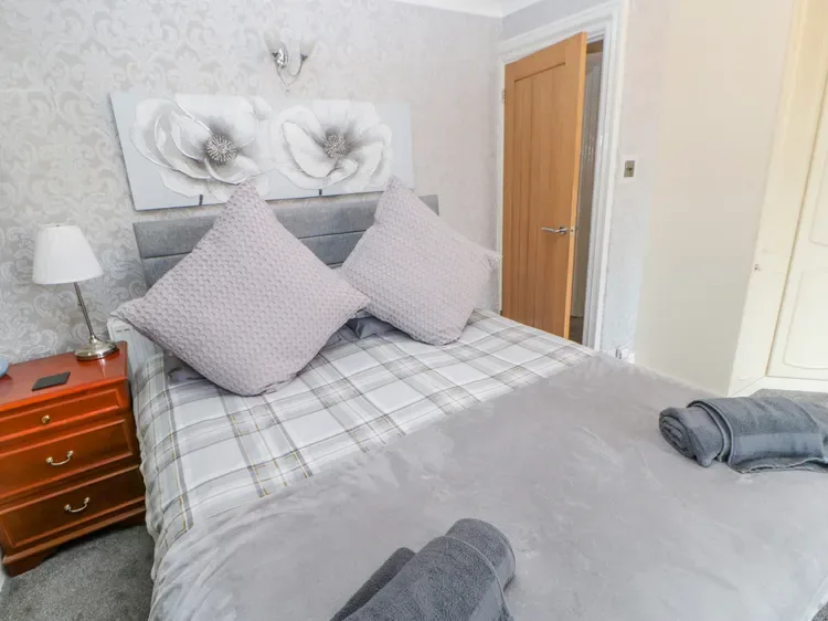 Un dormitorio con una cama tendida, cojines estampados y una mesita de noche de madera.