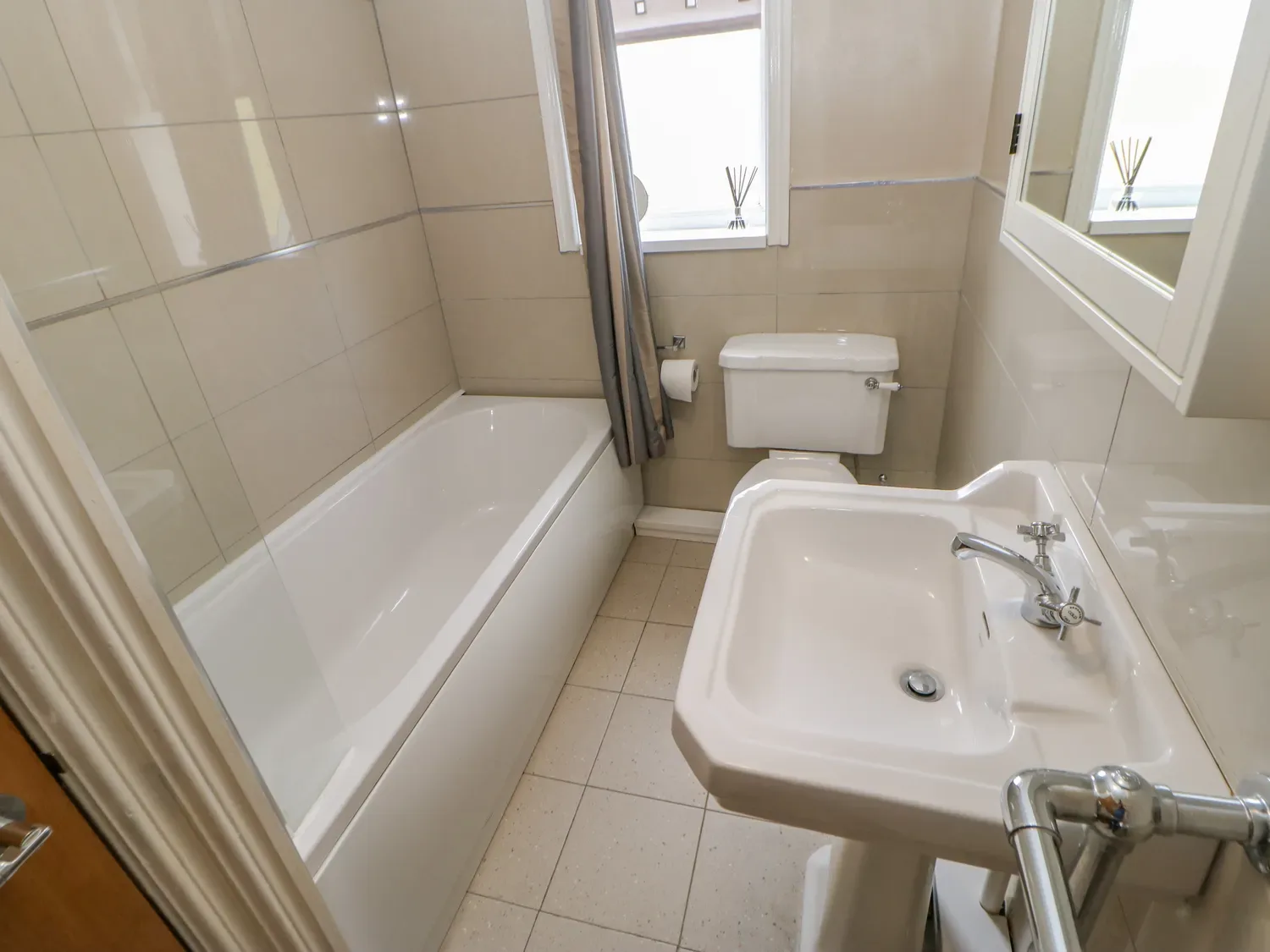 Un baño alicatado con bañera, inodoro y lavabo con pedestal.