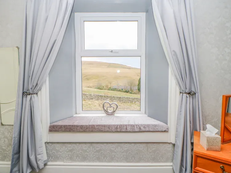Una ventana con cortinas da a colinas onduladas, con un adorno en forma de corazón en el alféizar.