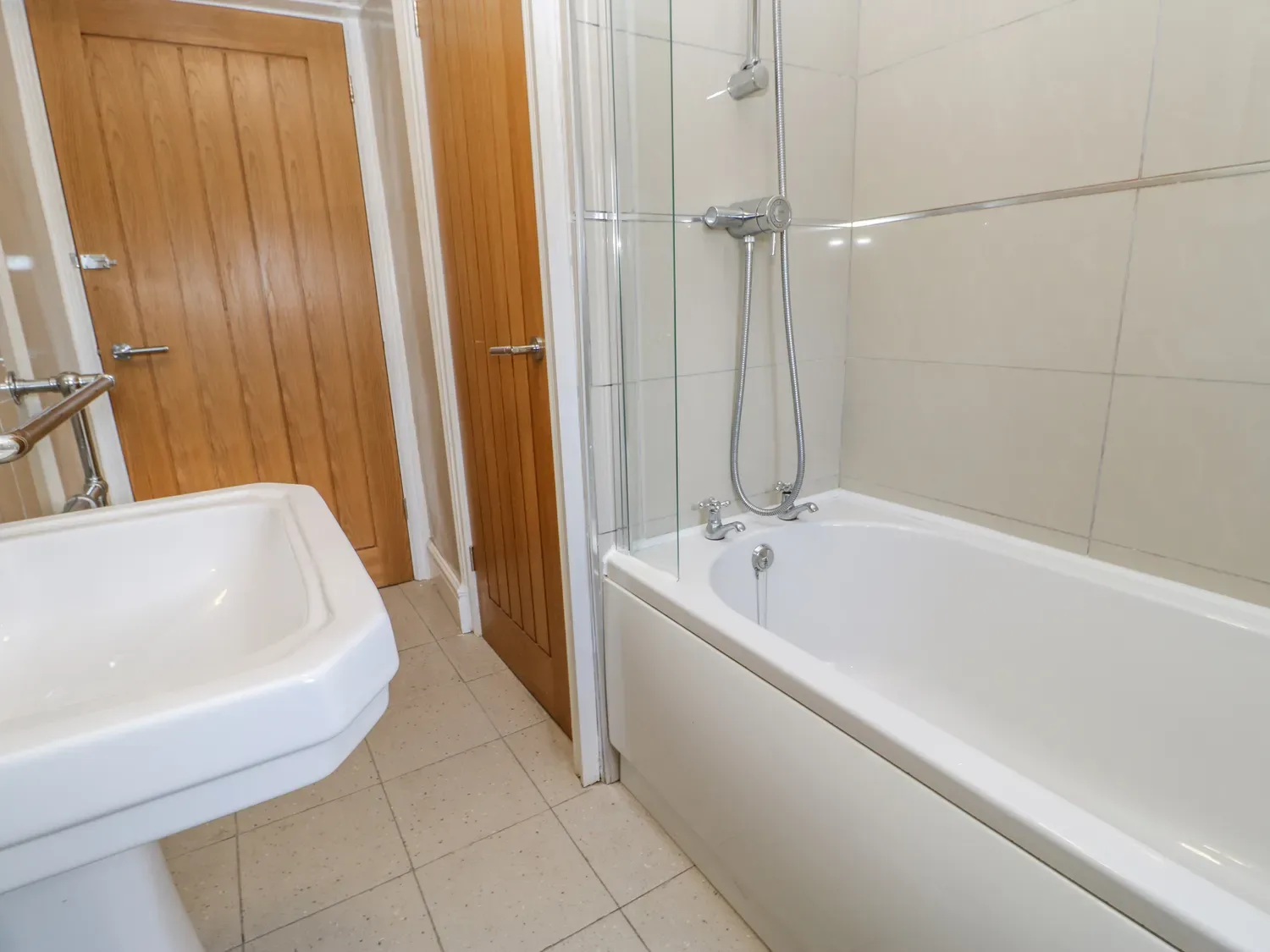 Un baño con bañera y ducha junto a un lavabo blanco y puertas de madera.