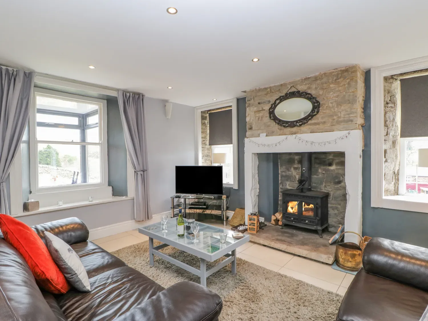 Un salón con sofás de cuero, una mesa de centro de cristal, un televisor y una chimenea con estufa de leña en 1 Braeside, en Cowshill, cerca de Wearhead