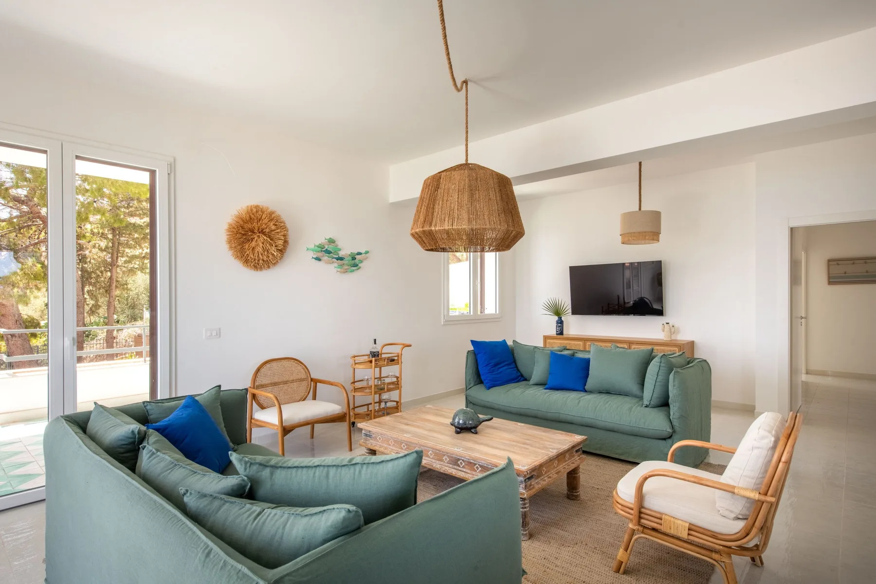 A bright living room with green seating, a wooden coffee table, and large windows.