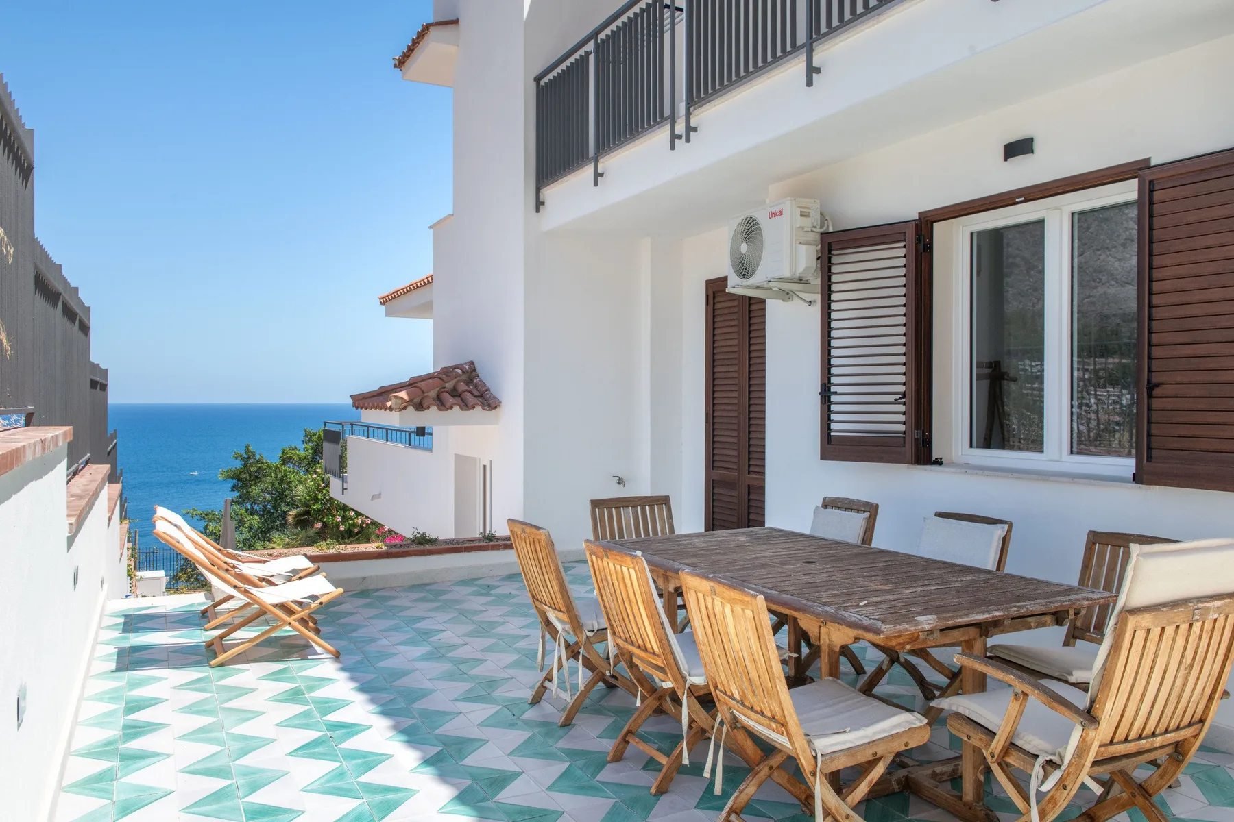 A tiled outdoor terrace has a wooden dining table and seating overlooking the sea.
