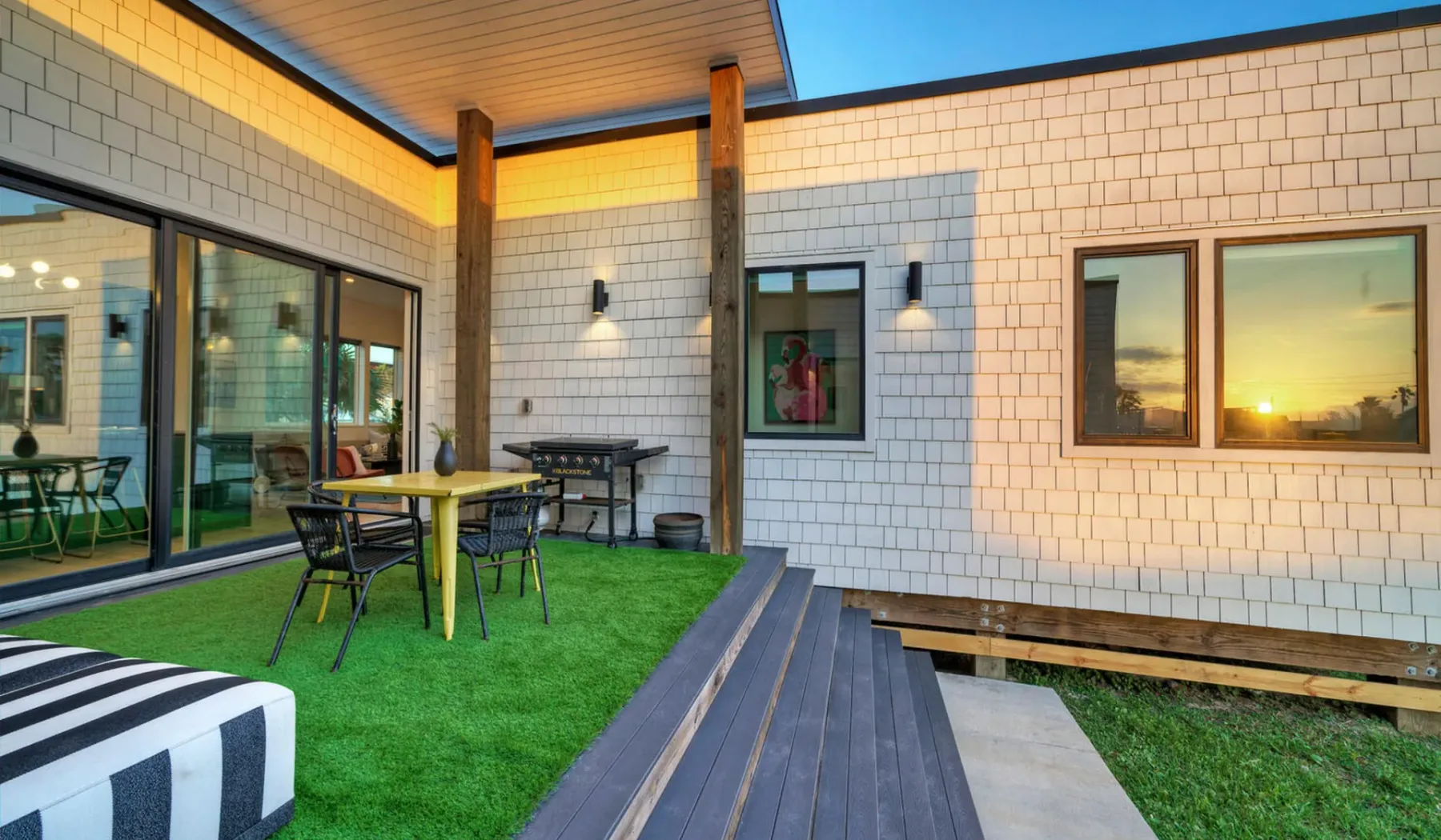 A covered outdoor patio with a dining table, chairs, and green lawn.