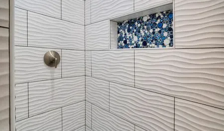 A tiled shower wall features a recessed niche with blue and white mosaic tiles.