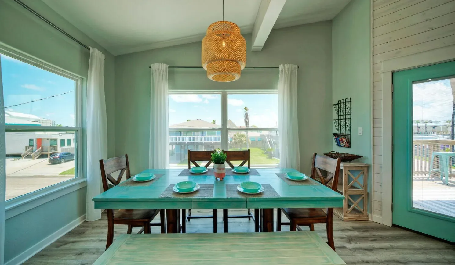 A dining area with a turquoise table set beside large windows.