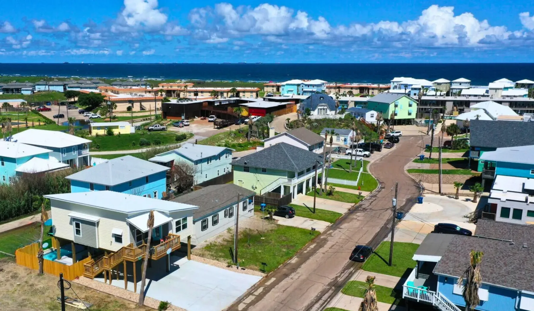 A coastal neighborhood of homes sits beside the ocean under a blue sky.
