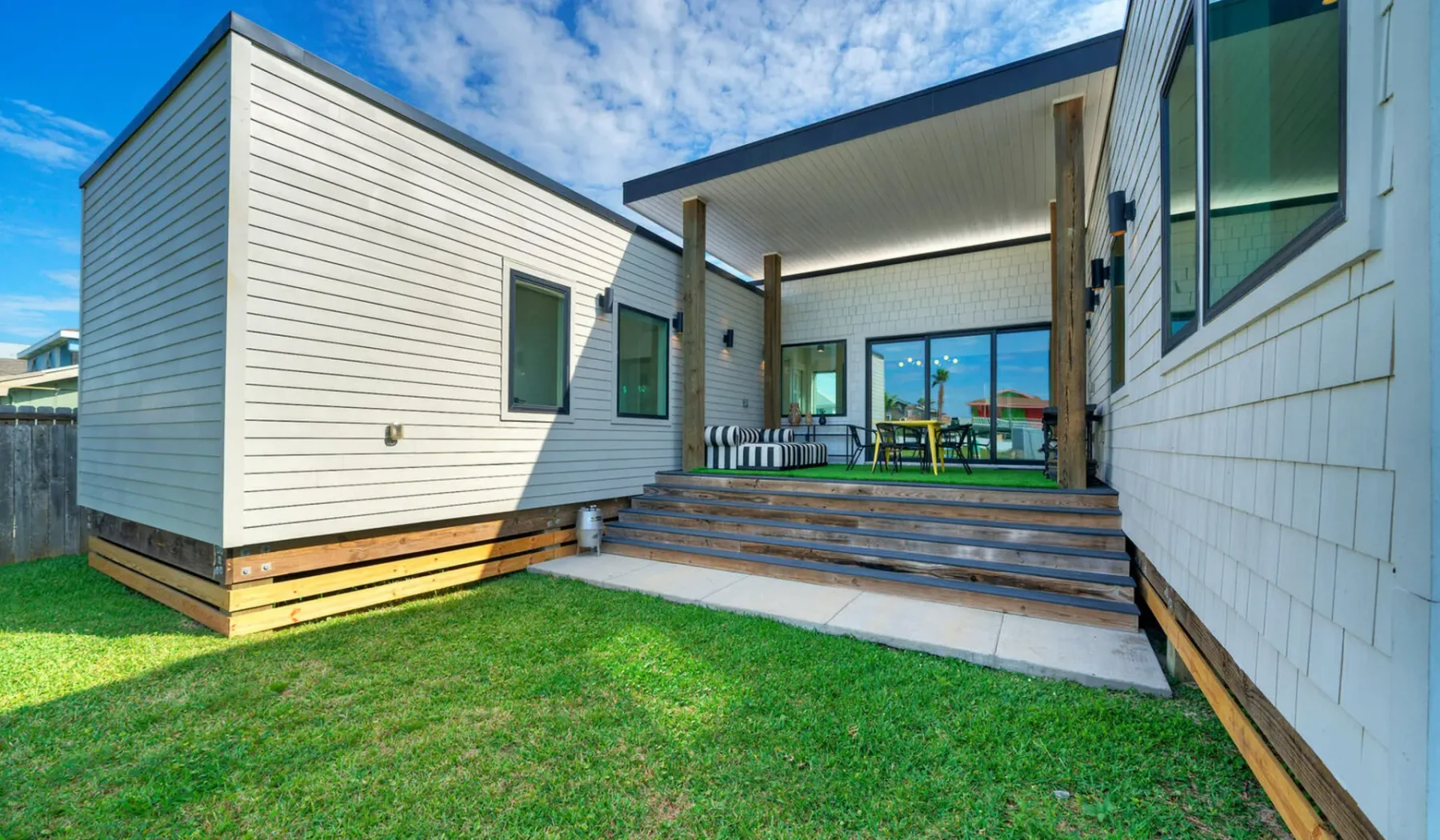 A modern house opens onto a covered patio with outdoor seating and a grassy yard.