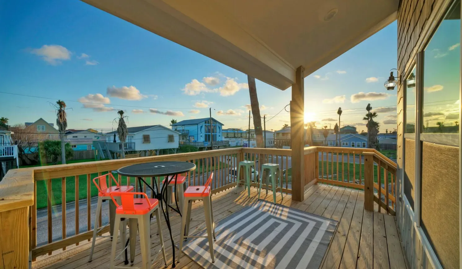 A covered deck with outdoor seating overlooks neighboring homes at sunset.