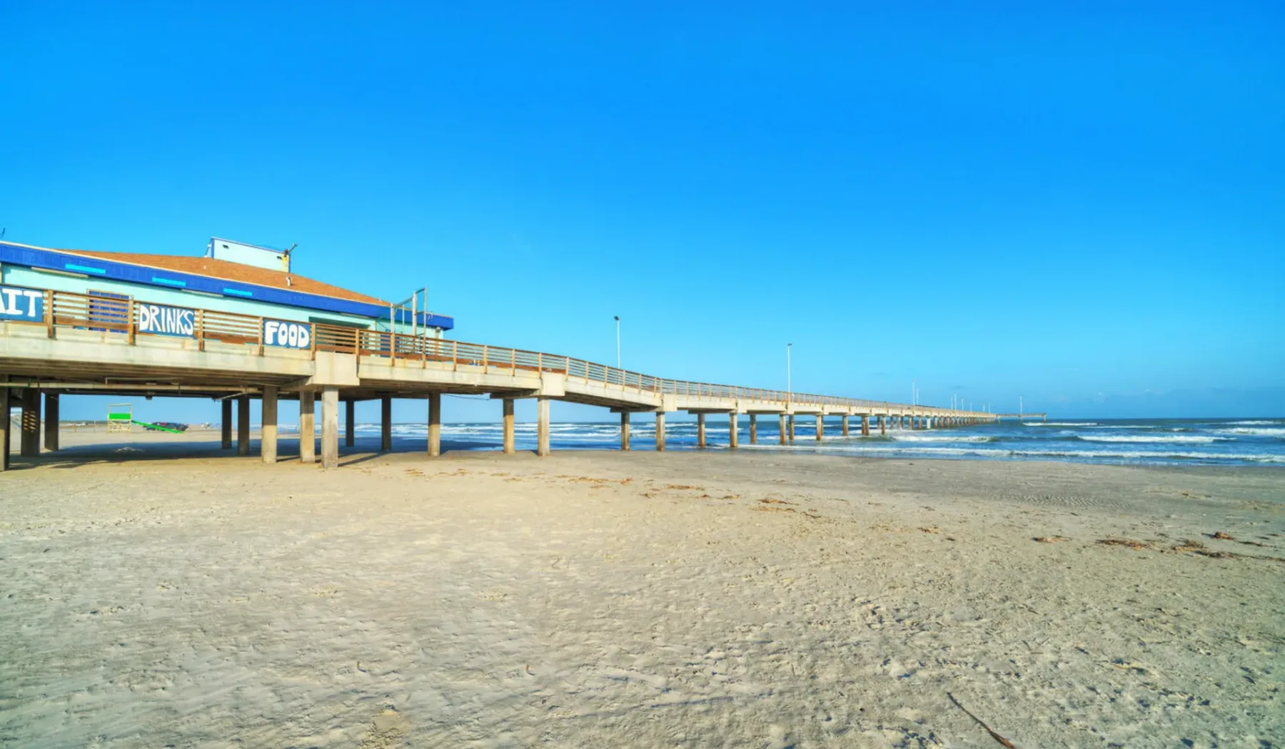 A sandy beach stretches beneath a long pier beside the ocean.