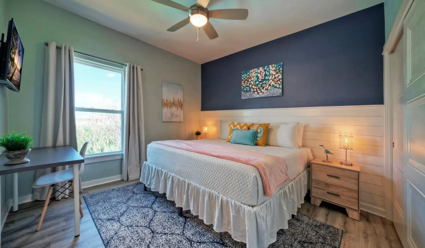 A bedroom with a bed, bedside tables, and a desk beside the window.