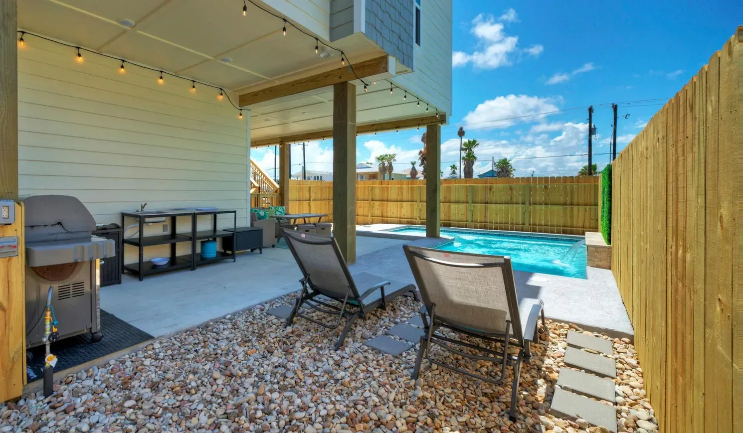 An outdoor patio has lounge seating beside a small pool and wooden fencing.