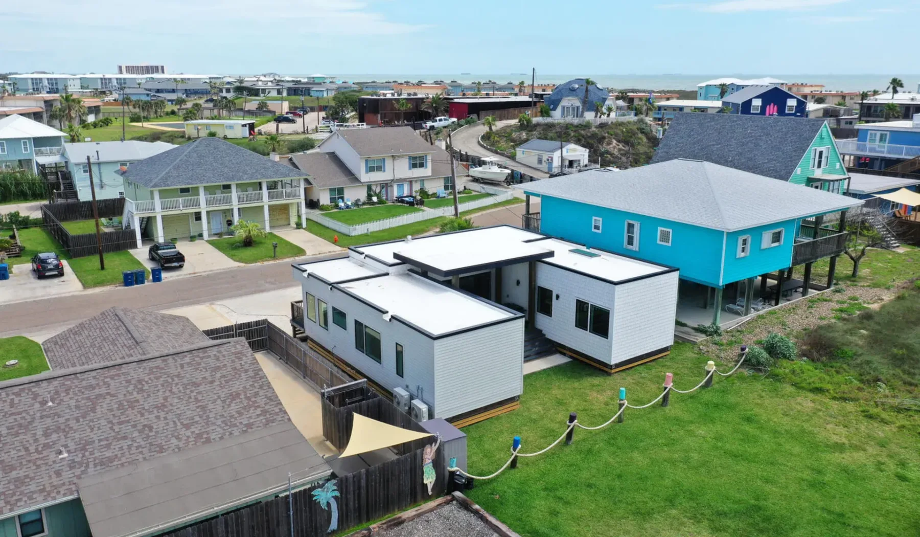 Aerial view of modern homes beside a bright turquoise house in a coastal neighborhood.