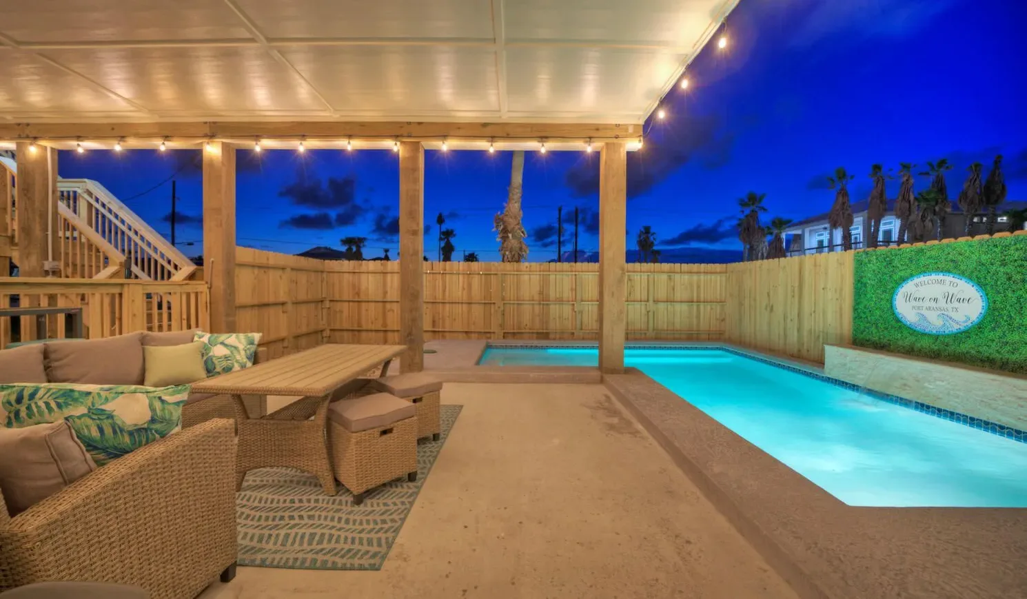 A covered outdoor patio with seating overlooks a lit swimming pool.