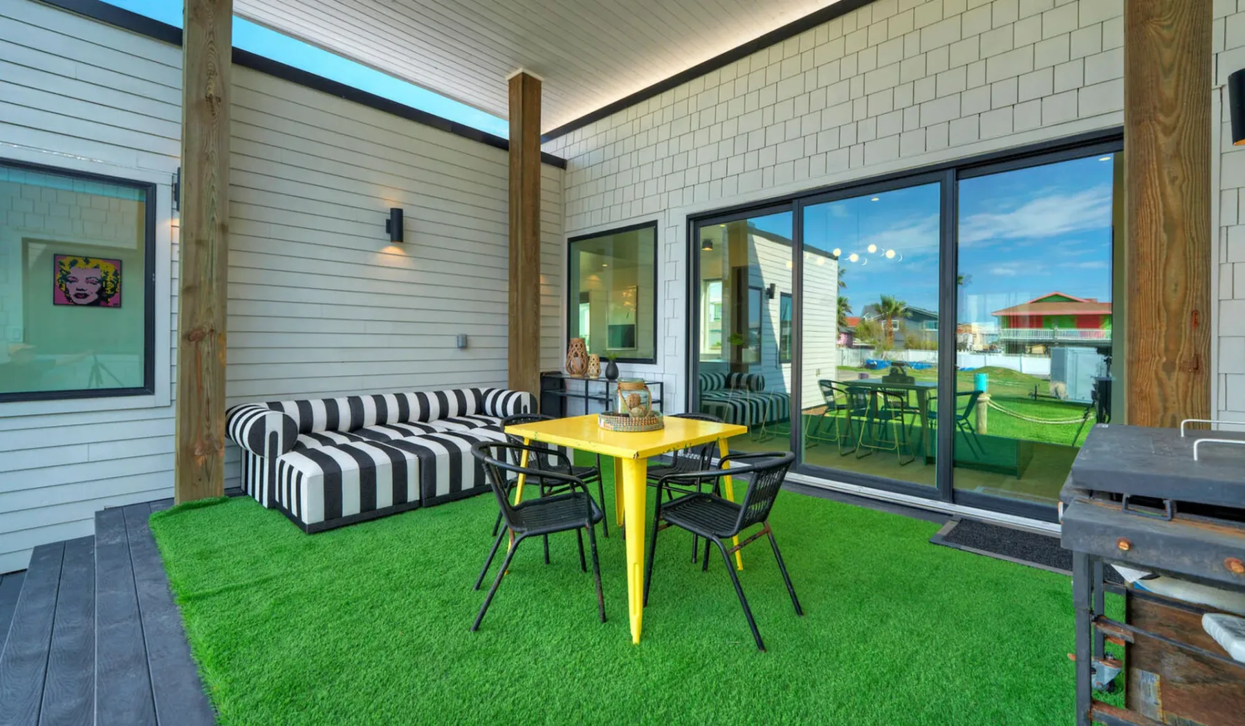 A covered patio with a yellow table, seating, and sliding glass doors.