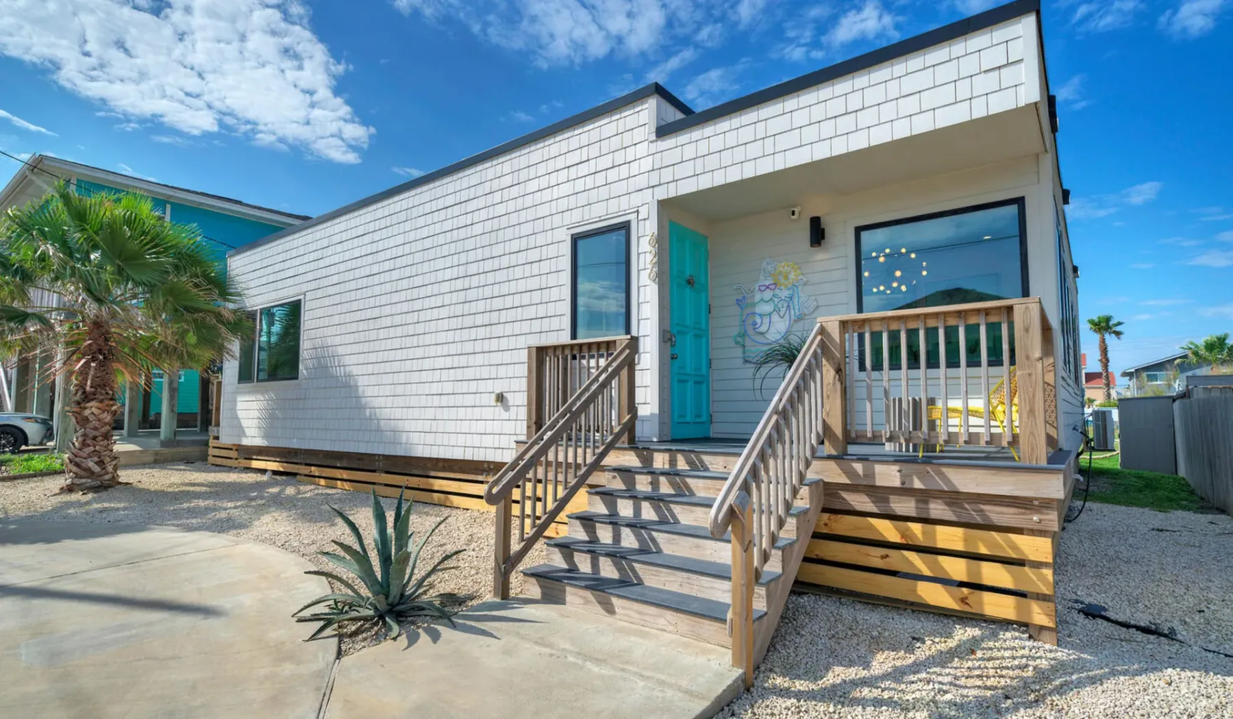 A modern white-sided building with a turquoise door, wooden steps, and a covered porch.