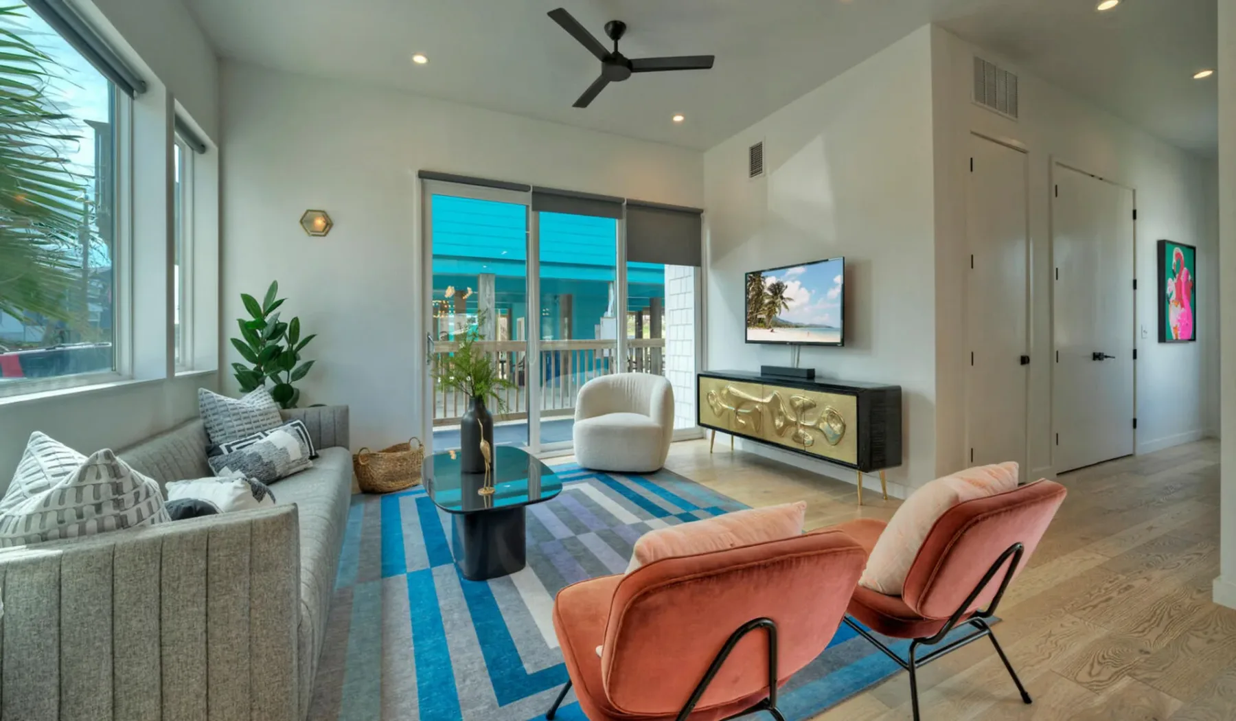 A bright living room with seating, a striped rug, and sliding glass doors.