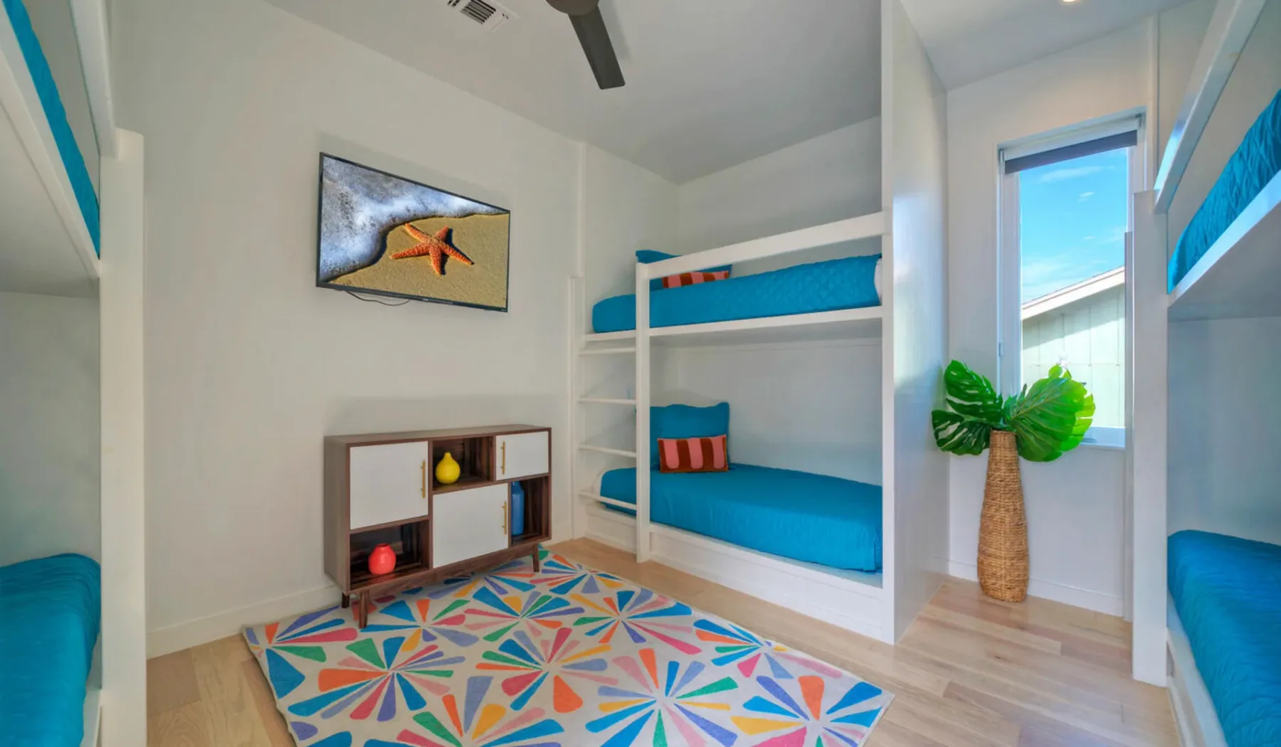 A bright bunk bedroom has teal bedding and a colorful geometric rug.