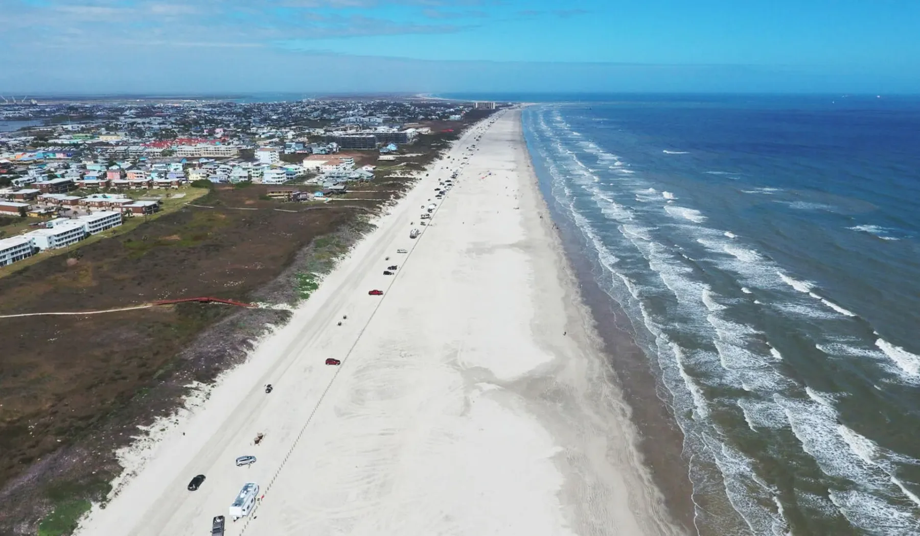 Aerial view of a long sandy beach beside the ocean and coastal buildings.