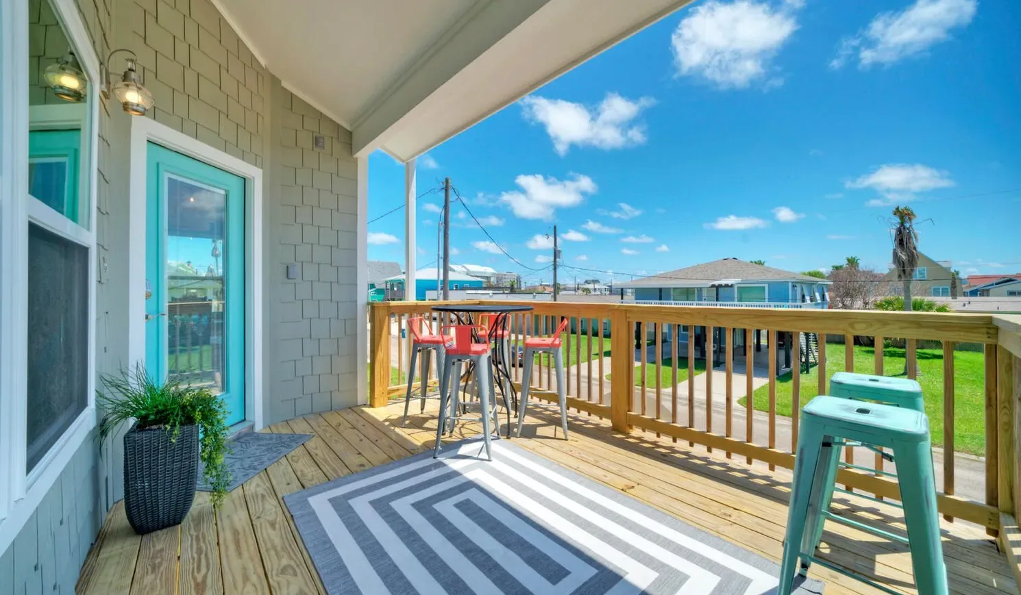 A covered wooden deck with outdoor seating overlooks a sunny neighborhood.