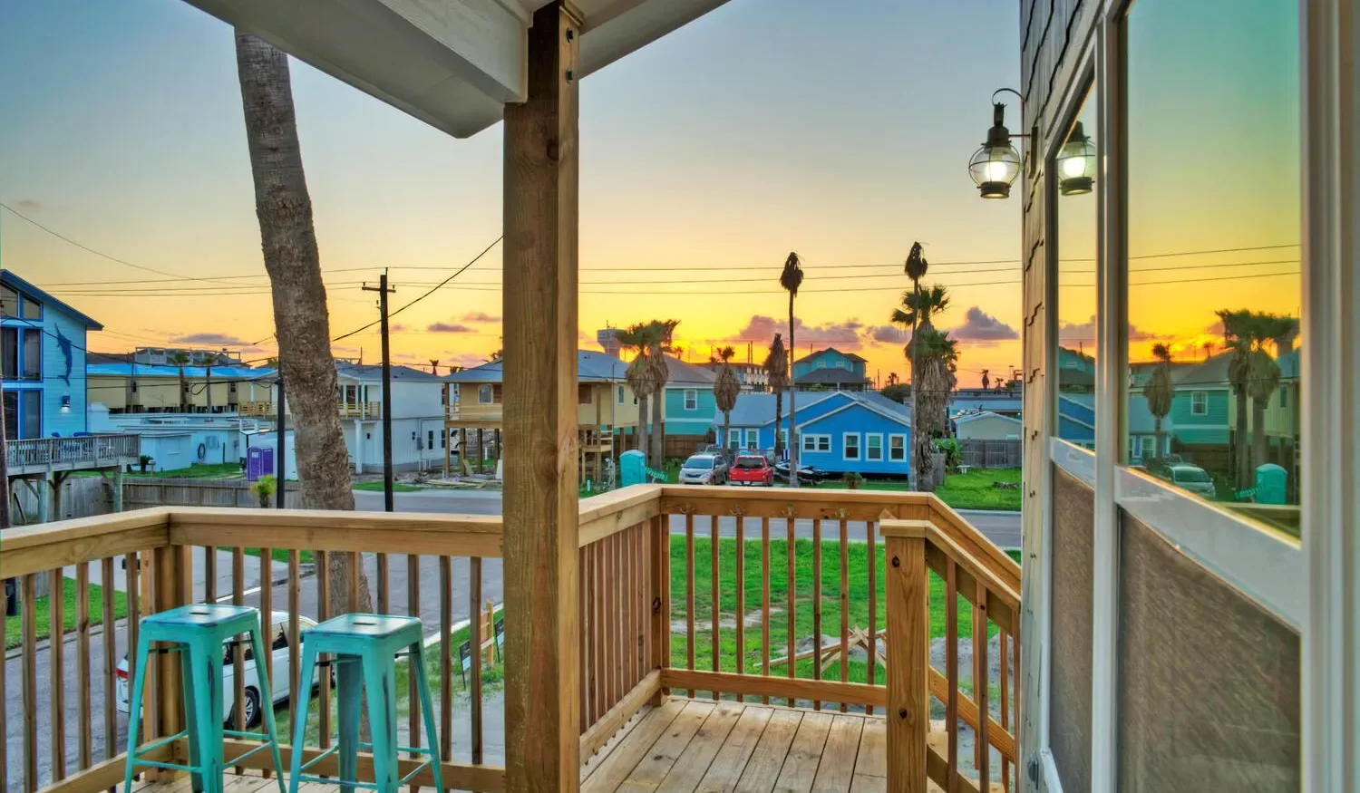 A wooden porch overlooks a residential street at sunset, with stools beside the railing.