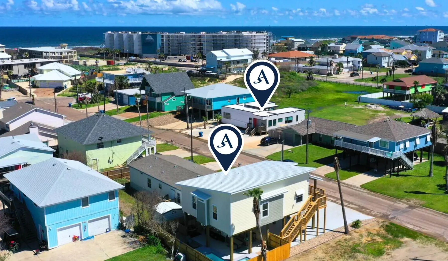Aerial view of a coastal neighborhood with low-rise homes and the ocean beyond.