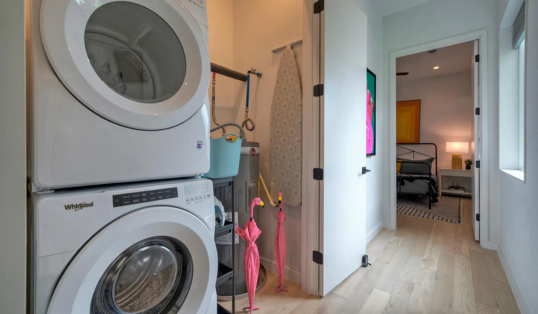 A hallway with stacked laundry machines and an open doorway to a bedroom.
