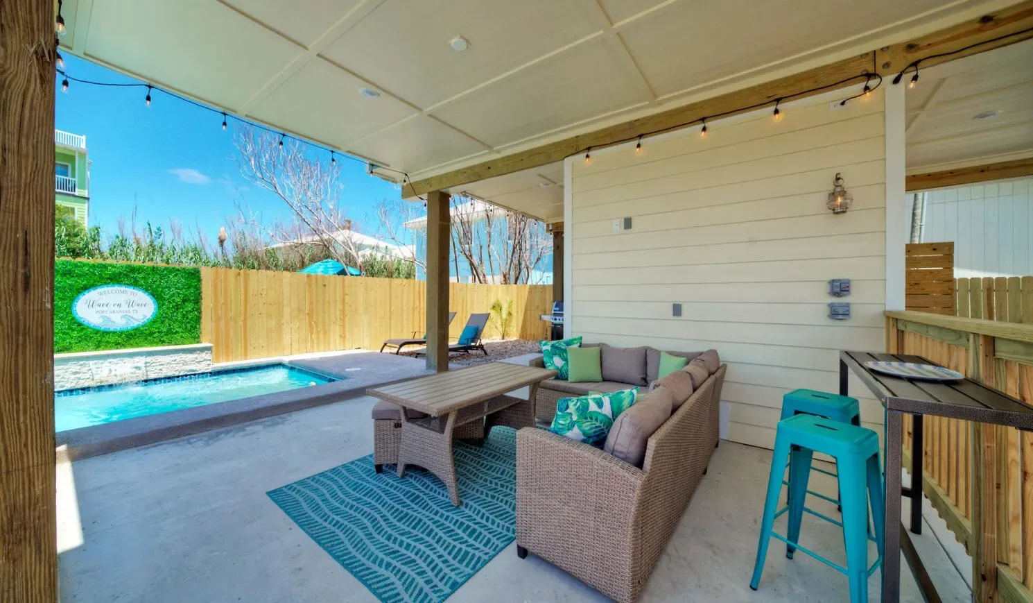 A covered patio with outdoor seating overlooks a swimming pool.