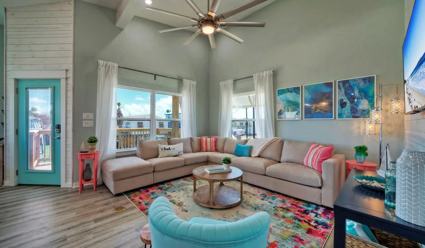 A bright living room with corner seating, colorful artwork, and a ceiling fan.