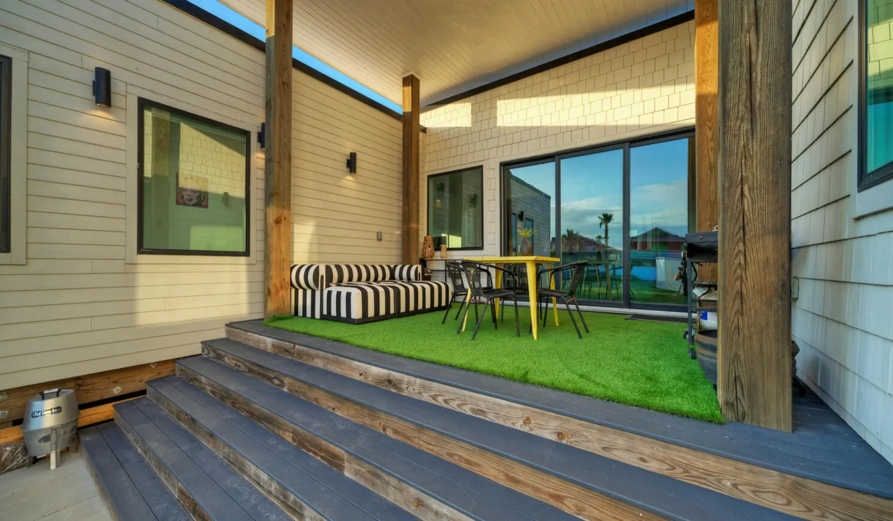A covered patio with outdoor seating and a table overlooks a grassy yard.