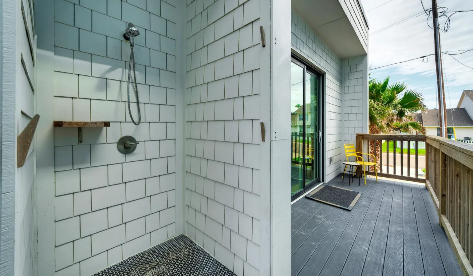 A tiled outdoor shower opens onto a wooden deck with a railing and seating.