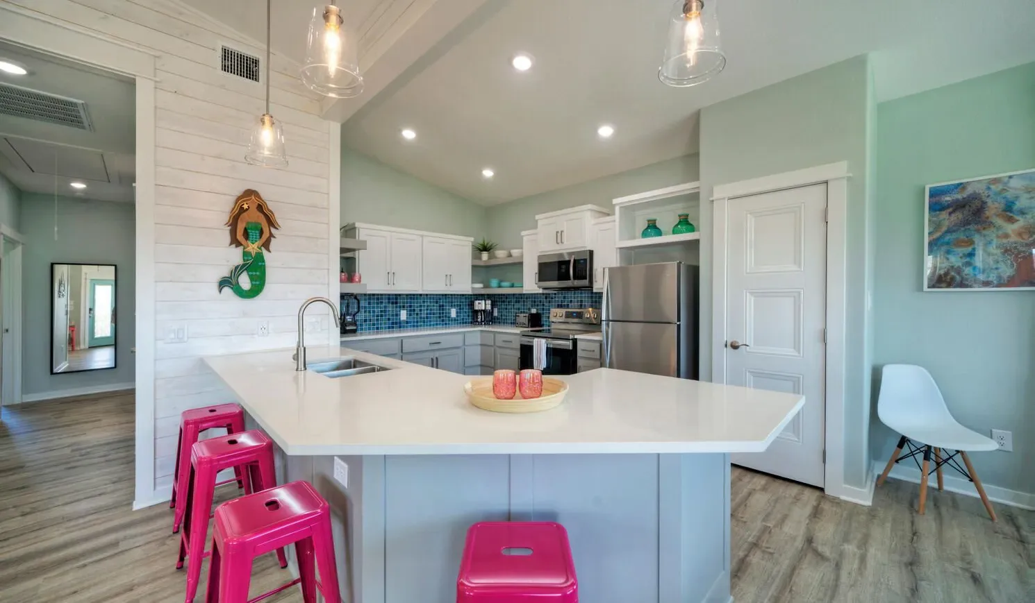 A bright kitchen with a large island, colorful stools, and stainless steel appliances.