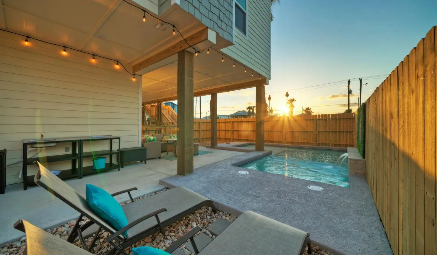 An outdoor patio with a small pool, lounge seating, and a wooden privacy fence.