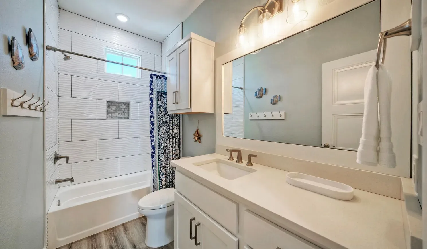 A bright bathroom with a bathtub, toilet, and long vanity beneath a large mirror.