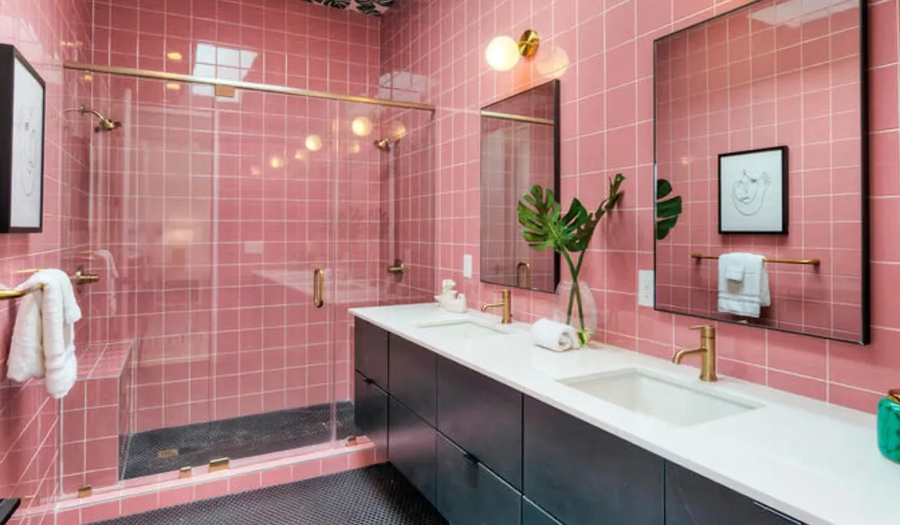 A pink-tiled bathroom with a long vanity, sink, and large wall mirror.