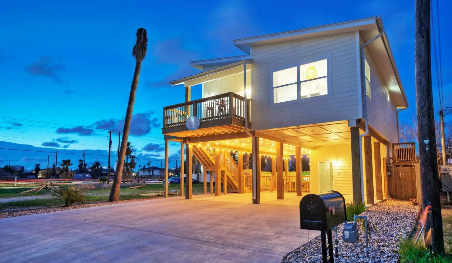 A raised house glows at dusk above a wide paved area.
