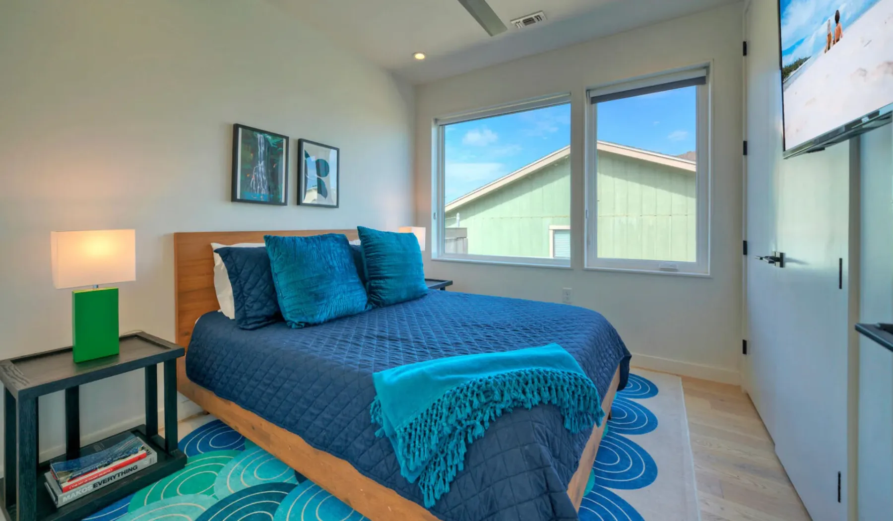 A bedroom with a bed dressed in blue bedding beside two windows.