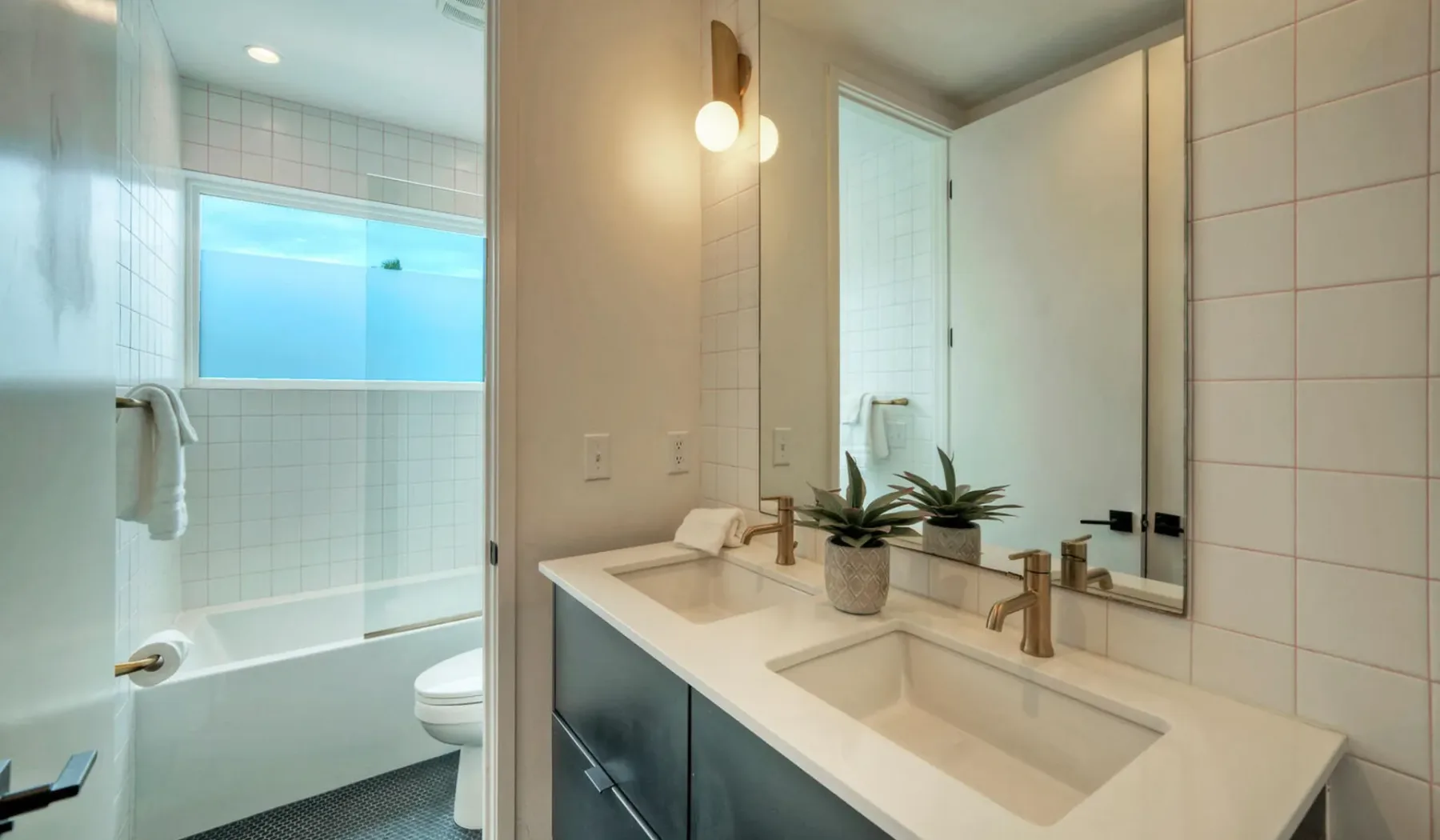 A bright bathroom with a bathtub, toilet, and double vanity.