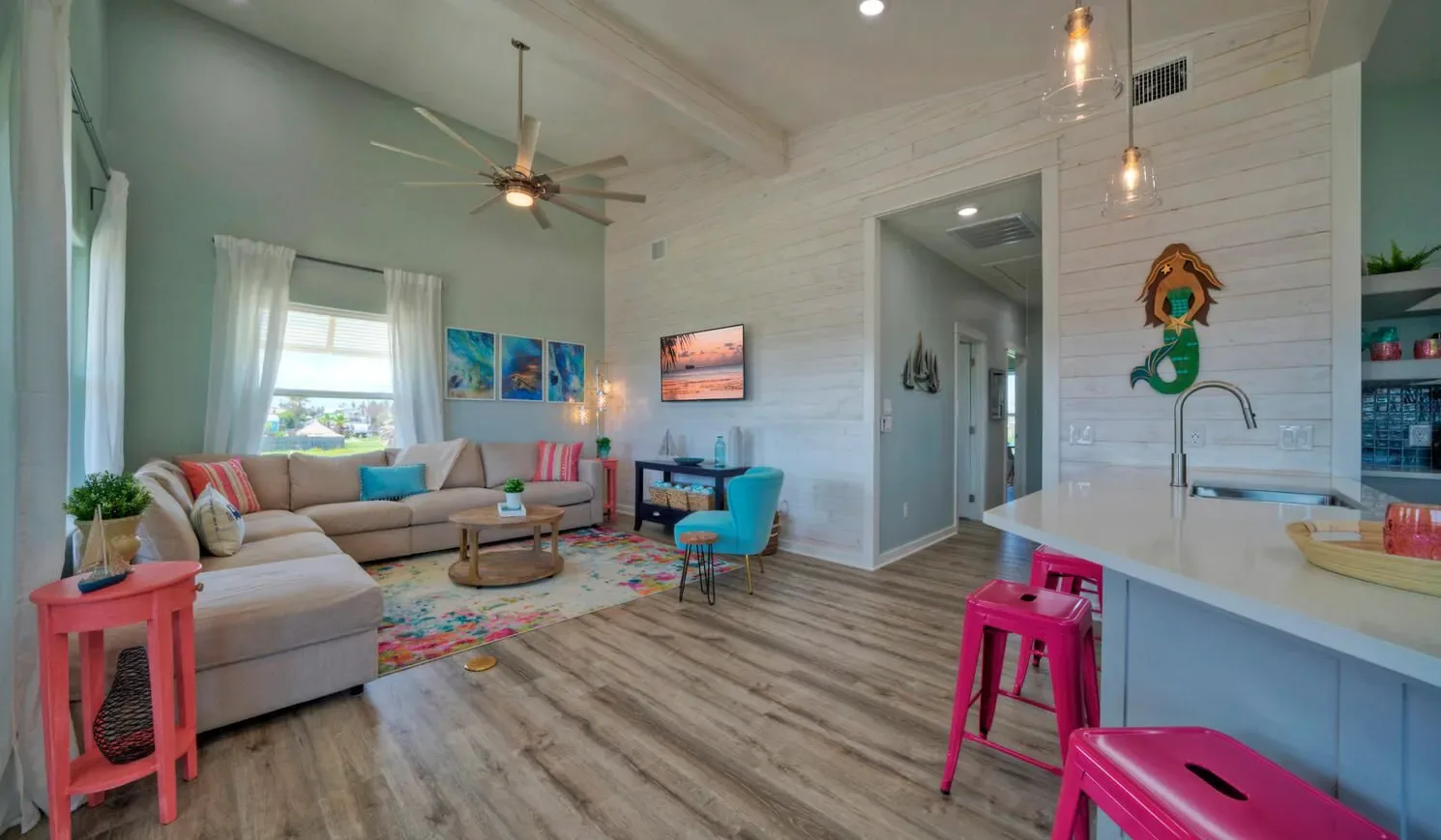 A bright living room with seating, a colorful rug, and a kitchen counter.