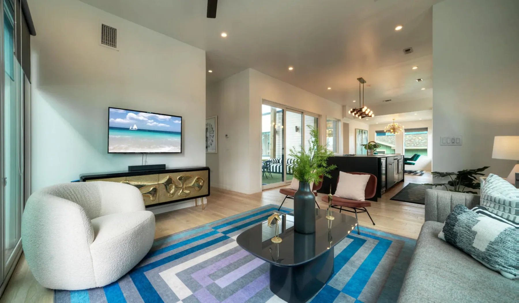 A bright living room opens into a dining area and kitchen, with colorful striped rug.