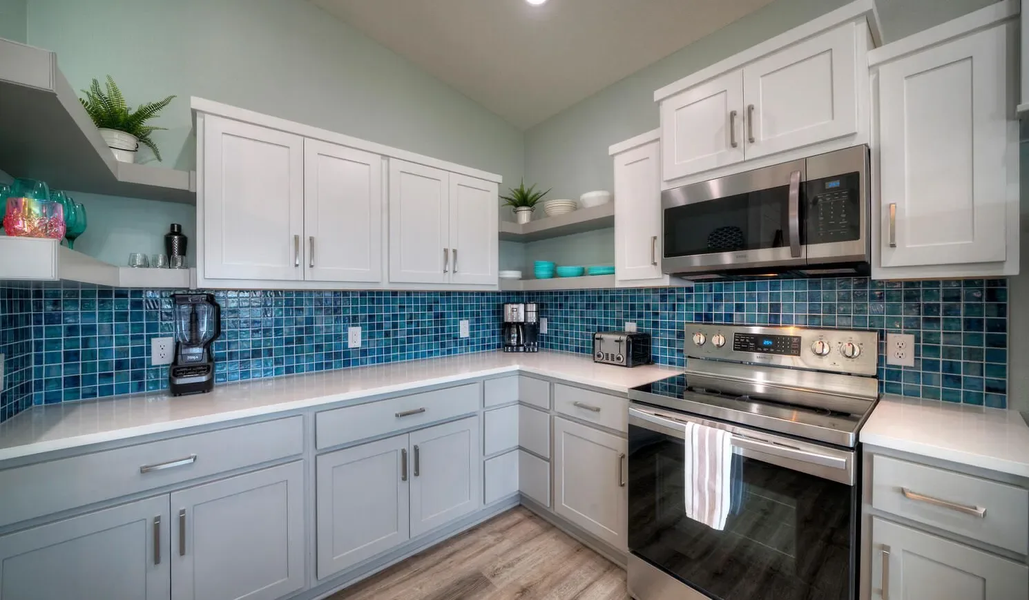 A kitchen with white cabinets, blue tile backsplash, and stainless steel appliances.