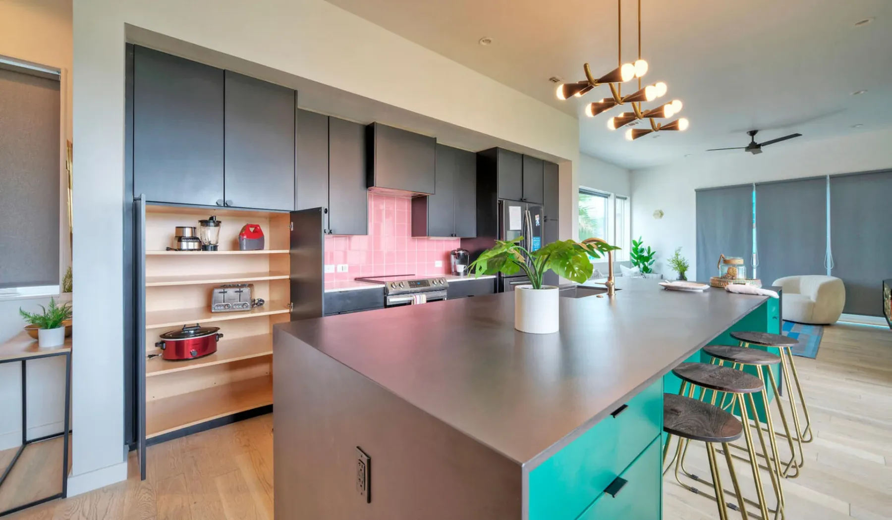 A modern kitchen with a large island, bar stools, and plants.