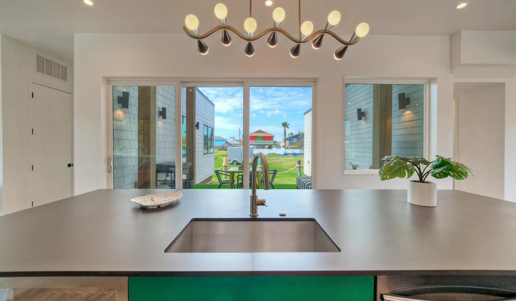 A bright kitchen with a broad island and windows overlooking a garden.