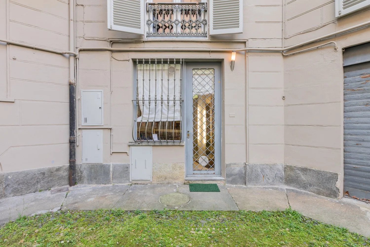 Entrada a nivel de calle con una reja metálica junto a una ventana enrejada.