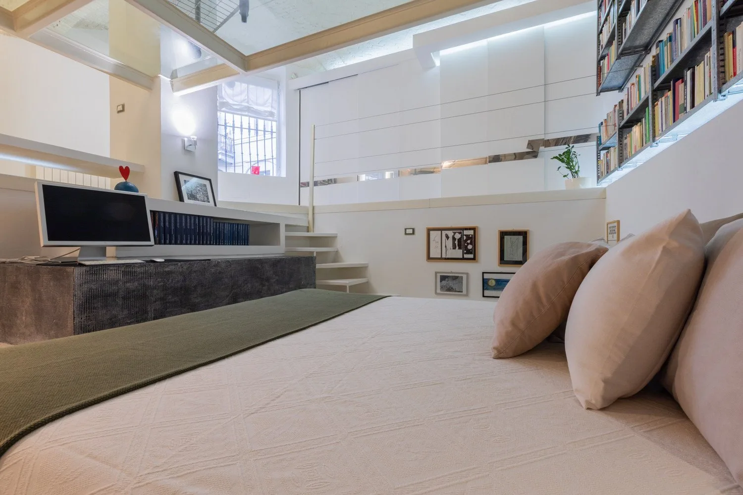 Un dormitorio tipo loft con una cama, un escritorio y estanterías en la pared superior.