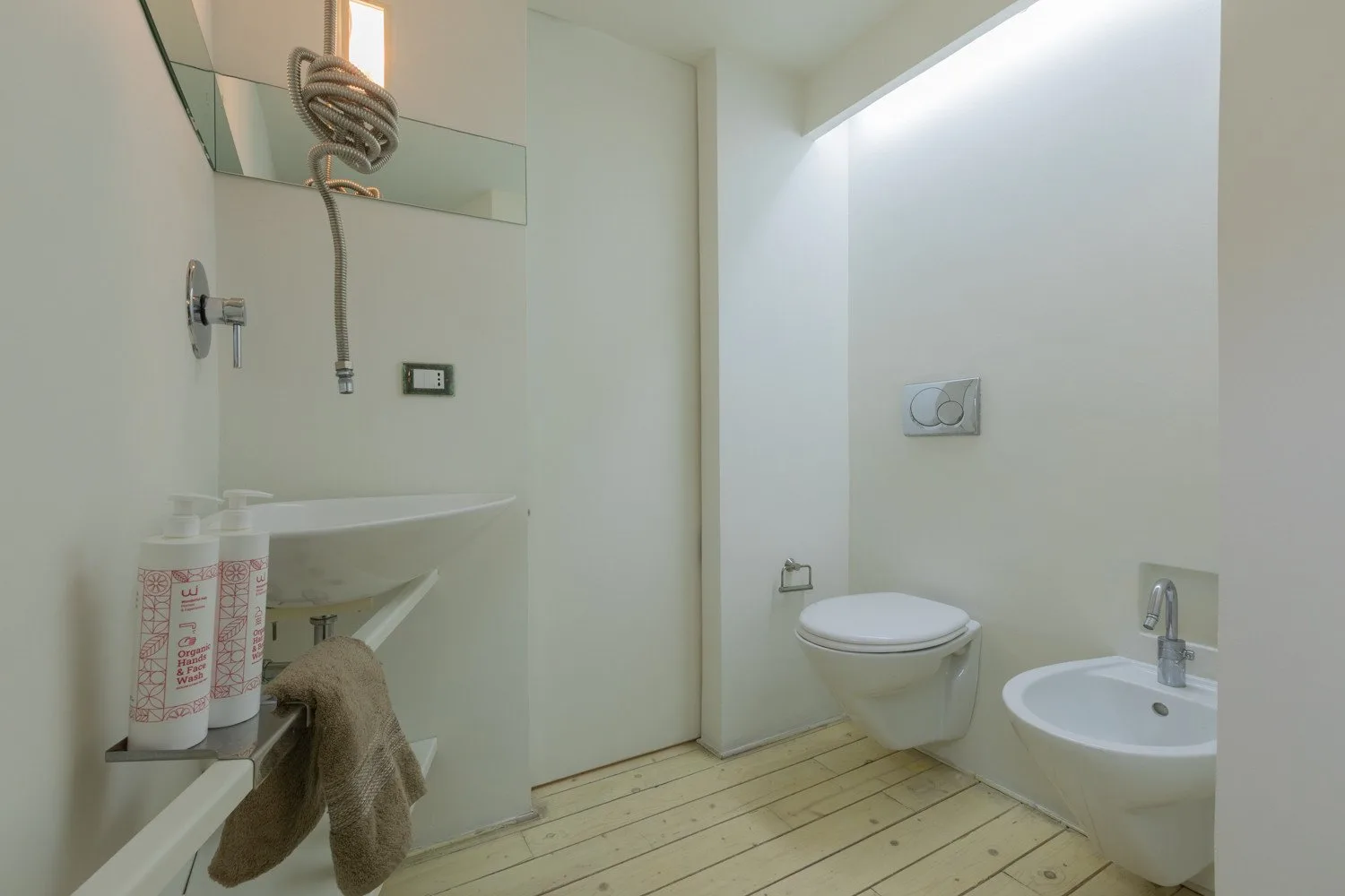 Un baño luminoso con un inodoro suspendido y un lavabo pequeño.