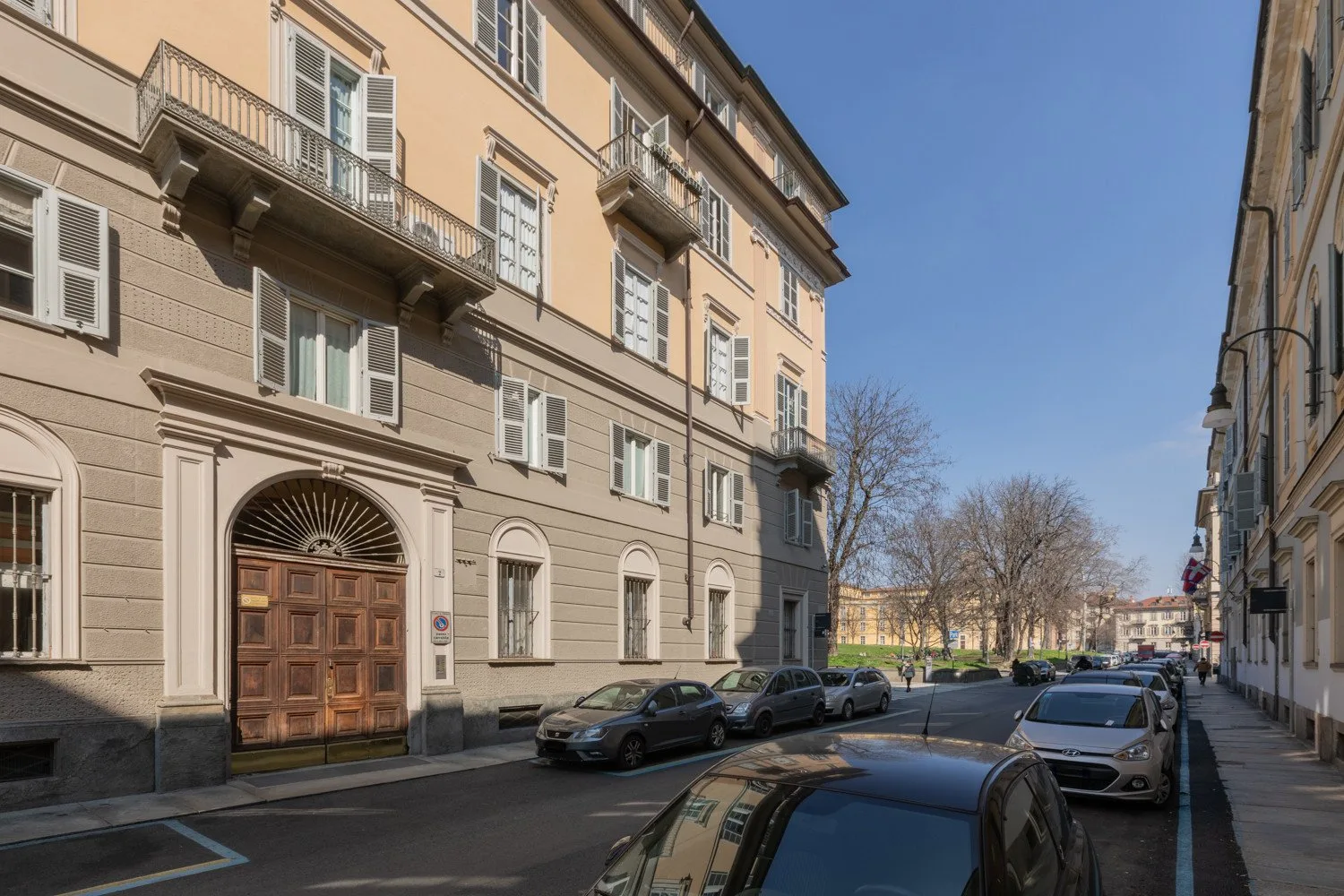 Una calle urbana con coches estacionados junto a un edificio de varias plantas con balcones.