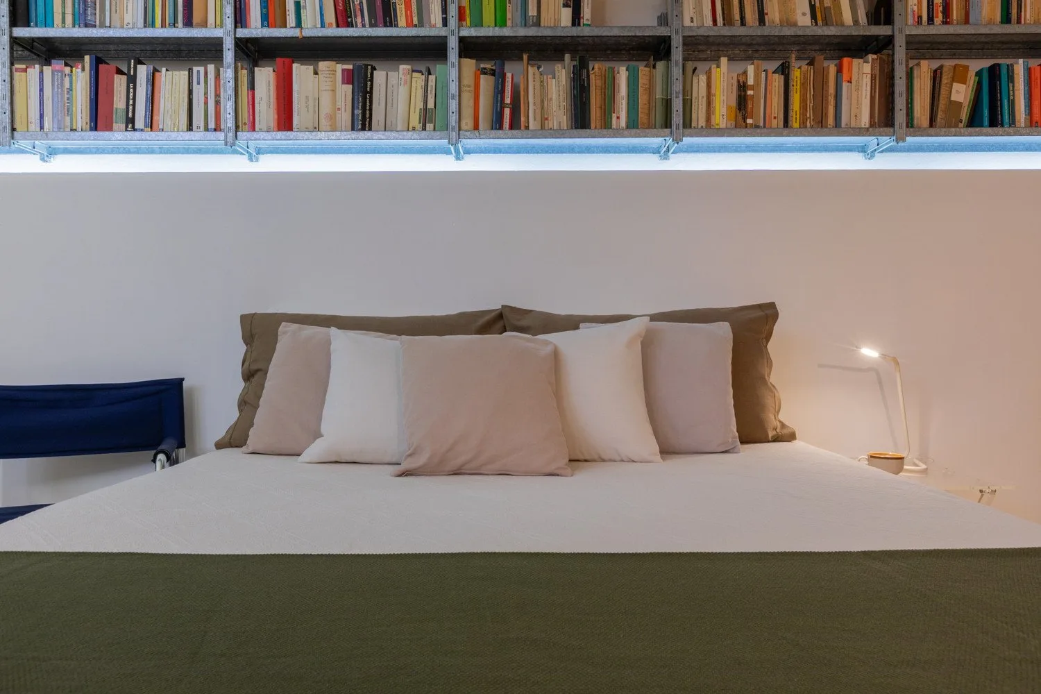 Un dormitorio con una cama bien arreglada bajo estantes llenos de libros.