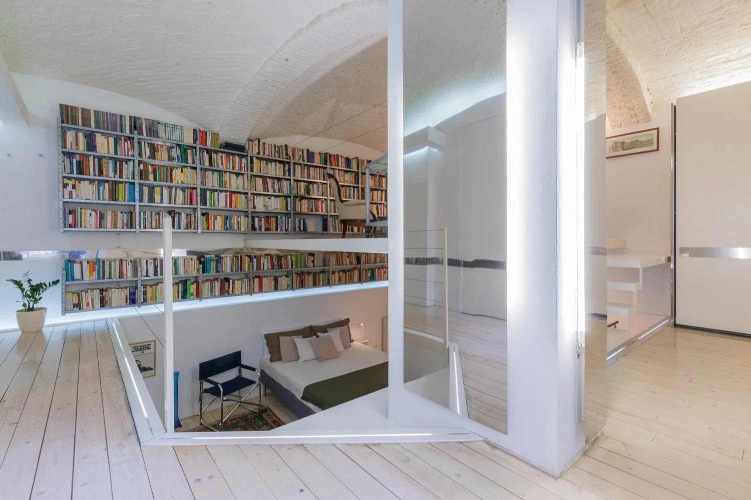 Una luminosa sala tipo loft tiene estanterías sobre una zona de estar y una mampara de vidrio.